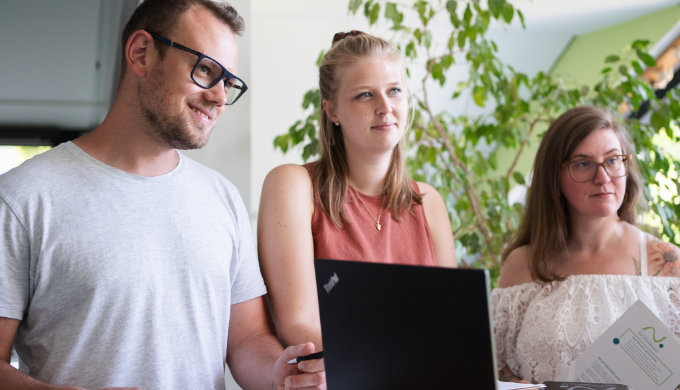 3 Studierende in einem Gespräch, stehend an einem Tisch