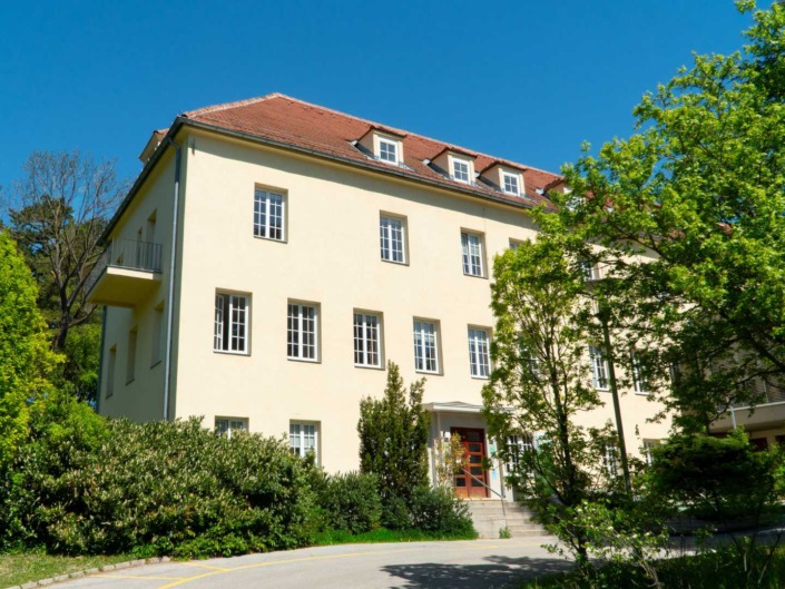 © Alexander Stadler Vorderansicht der Hochschule für Agrar- und Umweltpädagogik im Sommer mit Haupteingang, umgeben von grünen Bäumen und Sträuchern.