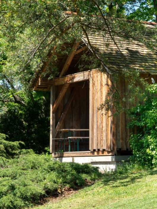 HAUP_Campus_©Alexander_Stadler_14 Holzhütte zum Verweilen im Hochschulgarten, umgeben von Sträuchern und Bäumen.