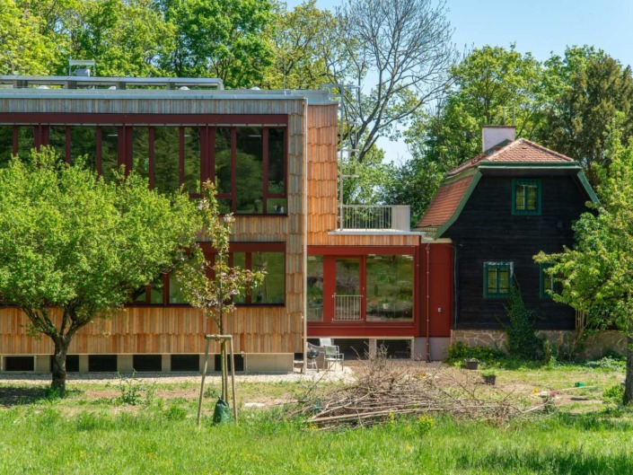© Alexander Stadler Vorderansicht des neu gebauten Gärtnerhaus der Hochschule für Agrar- und Umweltpädagogik im Sommer umgeben von Bäumen, Sträuchern und Wiese.