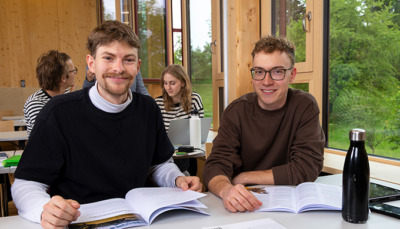 Erweiterungs-Studium-2-HAUP Zwei lächelnde, junge Studenten an der Hochschule für Agrar- und Umweltpädagogik in einem hellen, modernen Hörsaal.