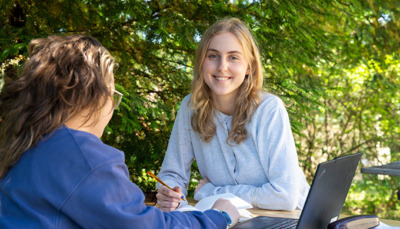 Umweltbildung-Beratung-Bachelor-GreenTransformation-1-HAUP Lächelnde Studentin beim Lernen draußen im grünen Campus der Hochschule für Agrar- und Umweltpädagogik.